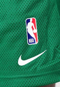 Pantaloni da basket a rete verdi con il logo NBA e il bordo bianco dello swoosh Nike.