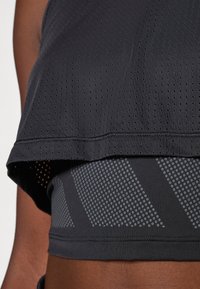 Black athletic tank top with perforated texture, layered over a fitted dark gray sports bra featuring a dotted pattern and diagonal stripes.