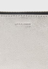 Zilveren leren portemonnee met een gestructureerd oppervlak, zwarte rits en debossed "ALLSAINTS" branding langs de bovenrand.
