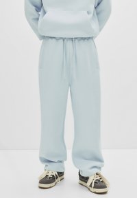 Lichtblauwe, verstelbare sweatpants in een relaxte pasvorm met zijzakken en een gestructureerde stof. Gecombineerd met grijs-witte sneakers.