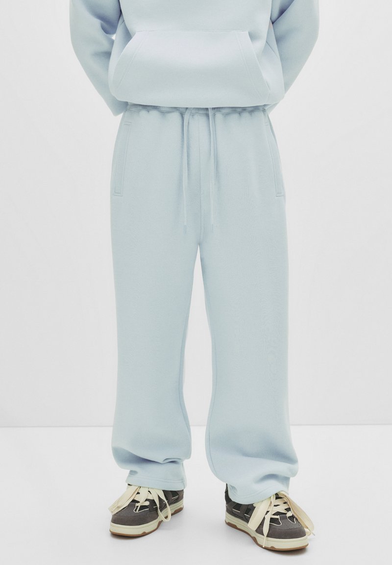 Lichtblauwe, verstelbare sweatpants in een relaxte pasvorm met zijzakken en een gestructureerde stof. Gecombineerd met grijs-witte sneakers.