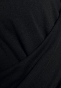 Svart tyg som visar en texturerad, stickad mönster med draperade veck, som framhäver mjukhet och släthet. Designen är enkel och utan utsmyckning.