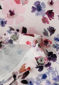 Bloemmotief stof in tinten roze, paars en blauw, met een drukknoopsluiting en delicate stiksels. Zacht, gestructureerd materiaal.