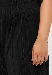 Close-up of a hand resting on a pleated black fabric, highlighting the texture and flow of the material.