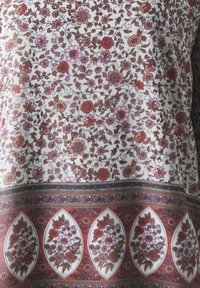 Tissu à motif floral avec des fleurs roses, rouges et brunes sur un fond blanc. Accentué par un design de bord contrastant.