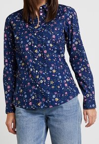 Navy button-up shirt featuring a floral pattern in pink, yellow, and blue. Long sleeves with a fitted design; cotton material.