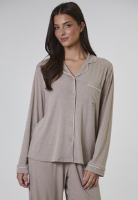Lichtbruine geribde pyjama-set met een knoopsluiting, een zak, lange mouwen en contrasterende witte bies. Zachte stoftextuur.