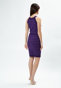 Vestido morado con un patrón geométrico texturizado, diseño ajustado, estilo sin mangas y dobladillo a la altura de la rodilla, combinado con tacones de tira en el tobillo plateados.