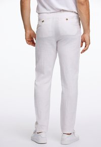 Pantalones de lino blancos con una tela texturizada, que cuentan con dos bolsillos traseros con botones dorados. Complementados con zapatillas blancas.