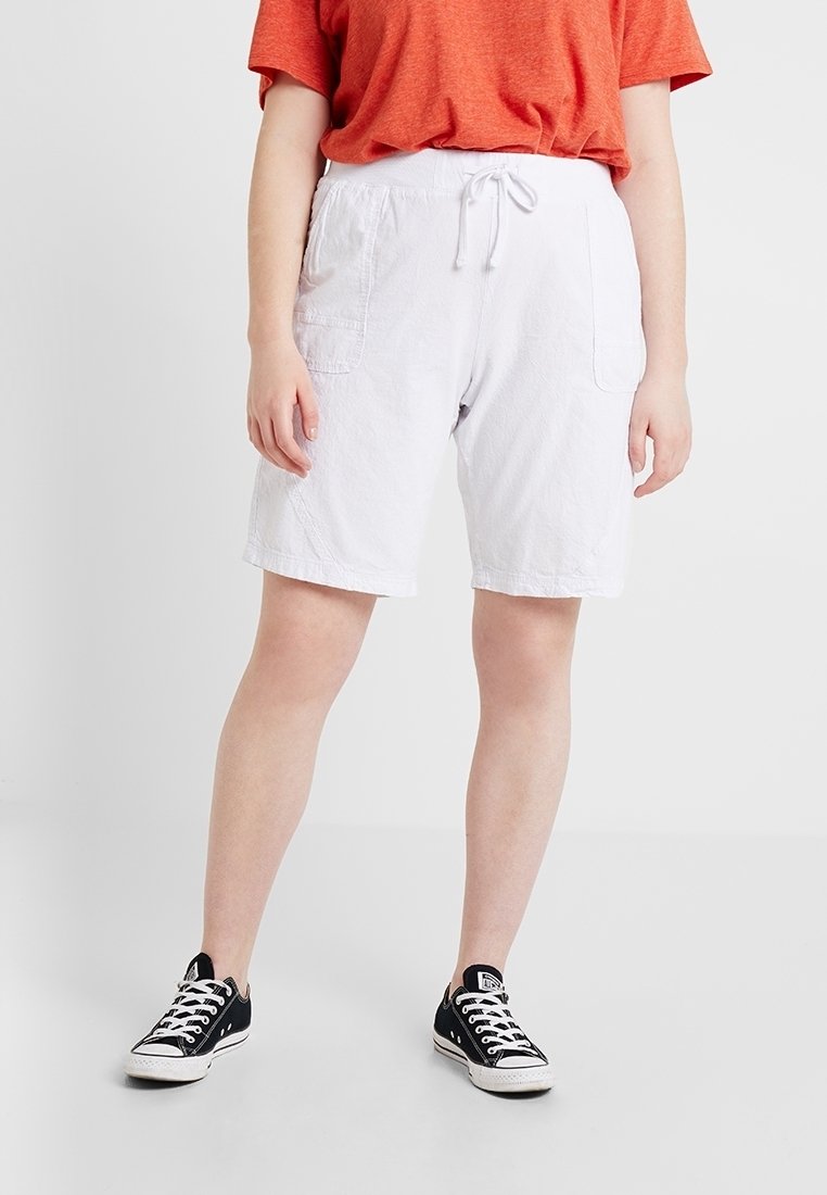 Shorts en coton blancs avec une taille élastique et un cordon de serrage, dotés de poches latérales. Associés à un t-shirt rouge ample et des baskets noires.