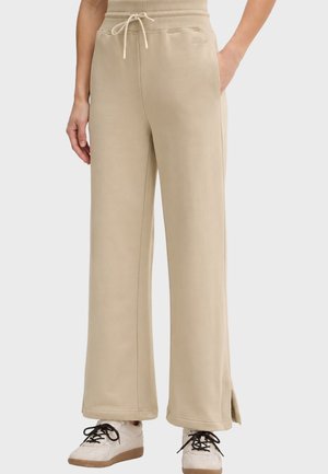 Pantaloni della tuta beige a gamba larga con vita con coulisse, tasche laterali e spacchi laterali all'orlo, indossati con scarpe da ginnastica bianche.