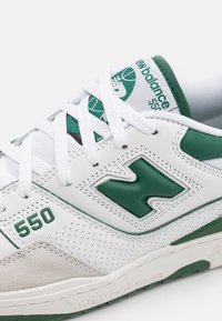 Las zapatillas New Balance 550 en blanco y verde presentan materiales de cuero y gamuza, un diseño perforado y un destacado logo "N" en verde.