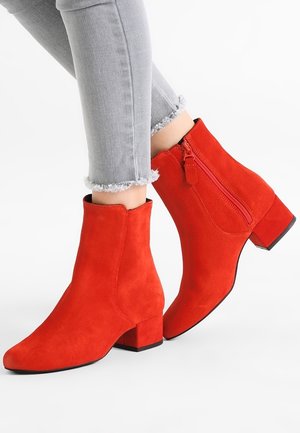 Bottines en daim rouge à talons blocs et fermetures éclair latérales portées avec un jean gris clair à ourlet effiloché.