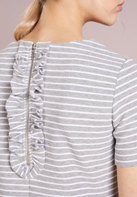 Haut rayé gris et blanc avec un accent froncé le long de la fermeture éclair à l'arrière. Manches courtes et tissu doux et ajusté.