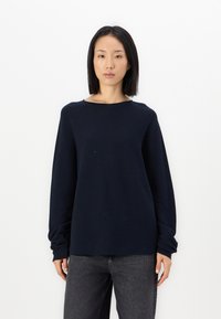 Marineblå langermet genser med avslappet passform, bred hals og teksturert stoff. Kombinert med mørke jeans. Enkel, minimalistisk design.