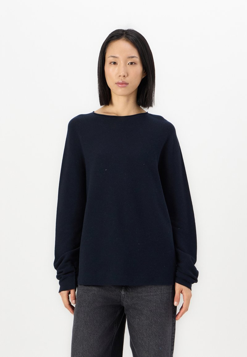 Marineblå langermet genser med avslappet passform, bred hals og teksturert stoff. Kombinert med mørke jeans. Enkel, minimalistisk design.