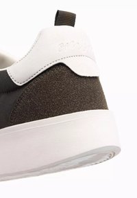 Sneaker med en brun mocka-häl och en vit läderöverdel. Har en texturerad yta och en kontrasterande vit gummisula.