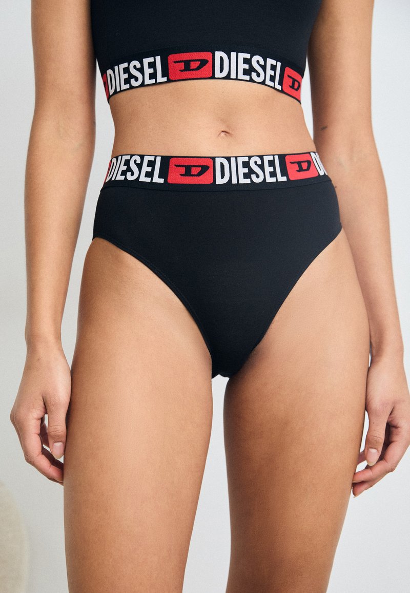 Culottes noires en coton taille haute avec une ceinture logo "DIESEL" rouge et blanche et une texture lisse, arborant un design classique et minimaliste.