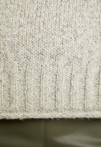 Gros plan sur un tissu beige tricoté avec ourlet côtelé posé sur une surface lisse en cuir vert olive.