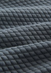 Tekstureret gråt stof med et quiltet mønster, der har en diamantform. Materialet virker blødt med synlige fibre og et let strakt udseende.