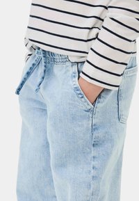 Pantalones de mezclilla azul claro con cinturilla elástica y cordón. La tela parece suave con un acabado ligeramente desgastado. Se ve una camiseta de manga larga a rayas.