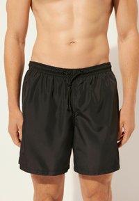 Bañador negro hecho de tejido ligero con cinturilla elástica y cordón ajustable. Presenta una textura simple y suave.