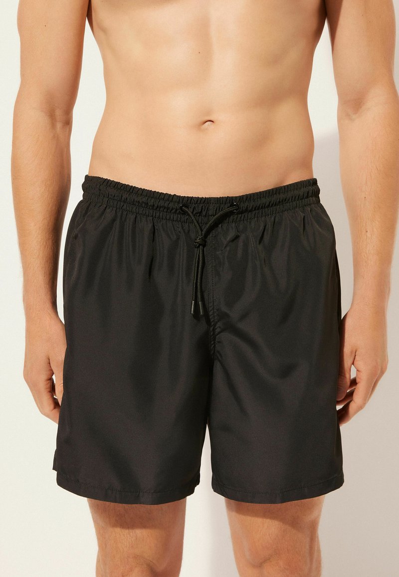 Bañador negro hecho de tejido ligero con cinturilla elástica y cordón ajustable. Presenta una textura simple y suave.