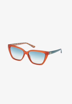 Ongemakkelijke oranje zonnebril met een geometrisch ontwerp, vervagende blauwe lenzen en een patroon op de glazen pootjes in bruine en oranje tinten.