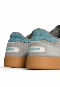 Sneaker scamosciate grigie e blu con suole in gomma, mostrano i talloni posteriori con il marchio "HOFF" in azzurro chiaro su pannelli bianchi.