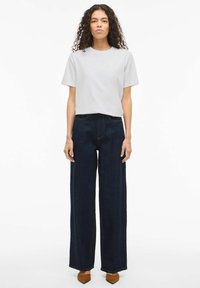 Lysegrå t-shirt i bomuld med korte ærmer, kombineret med mørkeblå jeans med vide ben og brune spidse hæle. Enkel design og afslappet pasform.