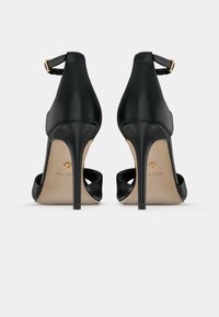 Black high-heeled shoes with a sleek design, leather material, open back, thin strap with gold-tone buckle, and a pointed toe.