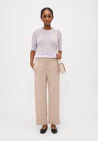 Light lavender knit sweater with short sleeves, paired with beige wide-leg trousers and black slip-on shoes. Small beige crossbody bag.