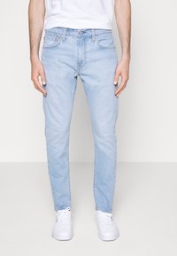 Ljusblå denimjeans med slim fit, med femficksdesign, knäppning och en blekt textur. Stylad med vita sneakers.