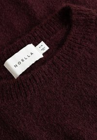 Tmavohnedý pletený sveter s rebrovaným okrúhlym výstrihom a bielou štítkom s nápisom "NOELLA" a "S/M VYROBENÉ V TALIANSKU."