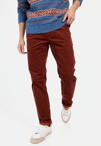 Rostfarbene Cordhosen, kombiniert mit einem blauen gemusterten Strickpullover und weißen Sneakers mit rosafarbenen Akzenten und schwarzen Details.