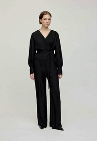 Czarny kombinezon z lekkiego materiału, z zapinanym przodem, długimi rękawami, paskiem w talii i szerokimi nogawkami. Prosty i elegancki design.