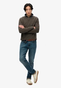 Sudadera gris con cuello redondo y detalle de punto cruz, combinada con jeans azules y zapatillas claras. Camisa de cuadros visible en el cuello.