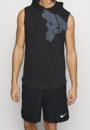 Mann trägt schwarzen ärmellosen Hoodie mit großem Wolfsgrafik auf der Brust und schwarze Nike-Shorts mit weißem Logo am linken Bein.
