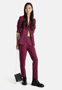 Completo giacca e pantaloni color bordeaux con rever a punta. Abbinato a stivali da combattimento neri e una borsa nera strutturata.