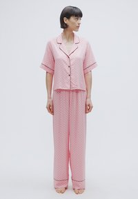 Σετ ροζ πιτζάμες με πουά, που περιλαμβάνει μπλούζα με κοντά μανίκια και κουμπιά και μακριά παντελόνια με ελαστική μέση και αντίθετες ραφές.