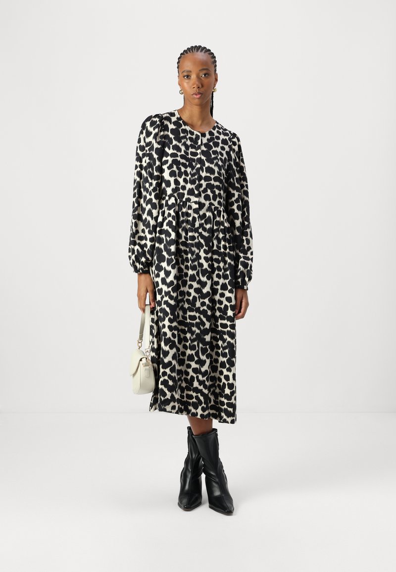 Schwarzes und cremefarbenes Leopardenmuster-Kleid mit langen Ärmeln, rundem Hals und gerafftem Bund. Kombiniert mit schwarzen Stiefeletten und einer weißen Tasche.