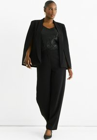 Black tailored pantsuit featuring a fitted blazer with cape sleeves and a sequined black top, complemented by black pointed flats.
