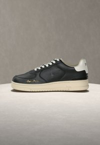 Μαύρο δερμάτινο αθλητικό παπούτσι χαμηλού τύπου με λευκά κορδόνια, κρεμ σόλα και κρεμ ταμπάκι στη φτέρνα, με διακριτικά χρυσά και ανάγλυφα λογότυπα της μάρκας.