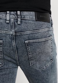 Jeans de denim de lavado oscuro con un ajuste slim, que cuentan con bolsillos traseros y una etiqueta de marca de cuero negro en la cintura.