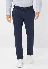 Marineblauwe broek van katoen, met een platte voorkant, zijzakken en een geweven riem. Gecombineerd met witte sneakers.