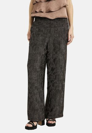 Mujer con pantalones anchos acanalados en negro y gris, con sandalias de plataforma negras y una parte superior sin mangas en capas color topo.
