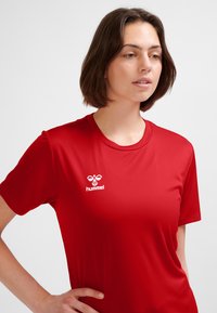 Rotes Sportshirt aus glattem Stoff mit rundem Ausschnitt und kurzen Ärmeln. Das Hummel-Logo ist deutlich in Weiß sichtbar.