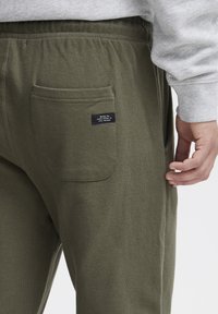 Olivgrüne Sweatpants mit strukturiertem Finish, ausgestattet mit einer Gesäßtasche und einem kleinen Markenetikett. Elastischer Bund für eine enganliegende Passform.