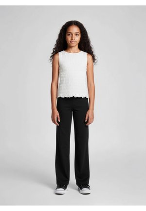 Top bianco senza maniche con un design strutturato e plissettato, abbinato a pantaloni larghi neri e scarpe da ginnastica nere. Sfondo neutro.