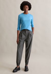 Blue long-sleeve shirt paired with gray patterned trousers featuring elastic cuffs and a belt. Black loafers complete the outfit.